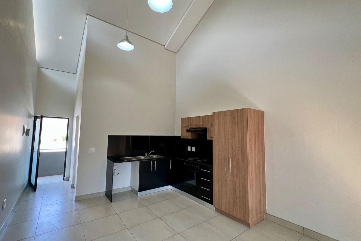 Modern kitchen area featuring high ceilings, built-in cabinetry, integrated oven, extractor fan, and tiled flooring in an open-plan layout.