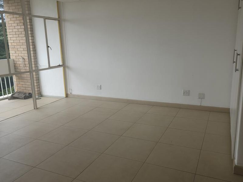 An empty, well-lit living area featuring neutral tiled flooring, built-in storage cupboards, and direct access to an outdoor balcony through a sliding glass door.