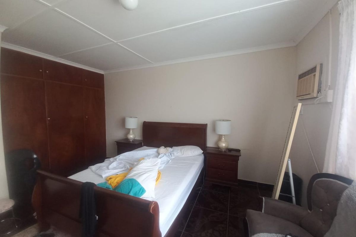 A bedroom featuring built-in wooden cupboards, tiled flooring, and a wall-mounted air conditioning unit.