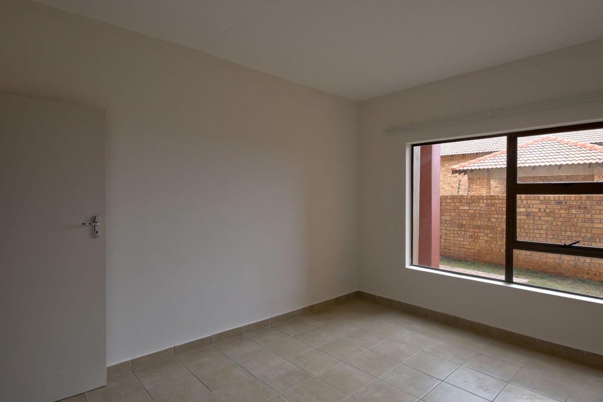 A clean, empty bedroom featuring neutral wall tones, tiled flooring, and a large window with an aluminium frame.
