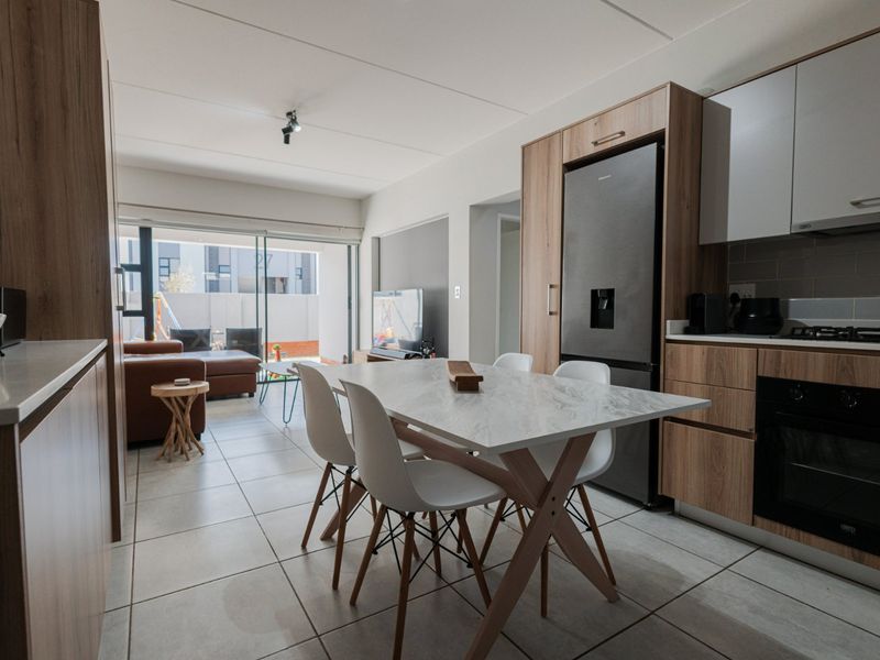 Modern open-plan living area featuring a contemporary kitchen with built-in cabinetry, stone countertops, and integrated appliances, flowing seamlessly to a patio through sliding glass doors.