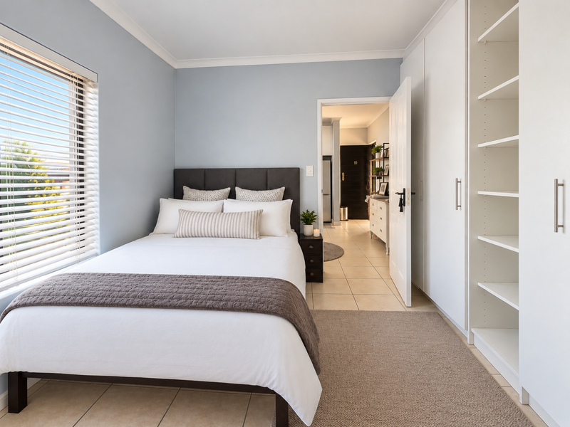 A well-maintained bedroom featuring built-in wardrobes, tiled flooring, and large windows with venetian blinds, offering a bright and functional living space.