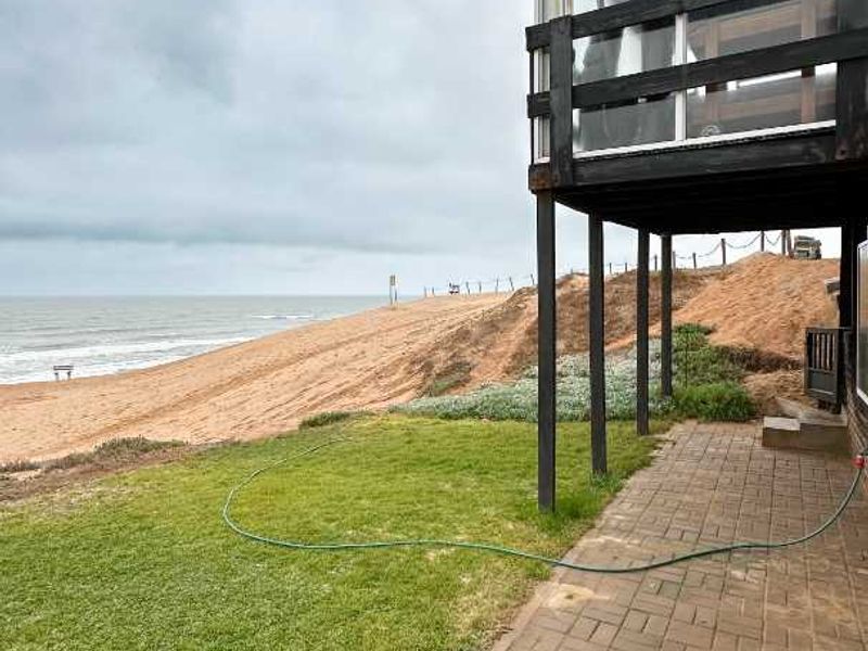 Rear exterior view of the townhouse featuring a paved patio, lawn area, and an elevated balcony overlooking the beach.