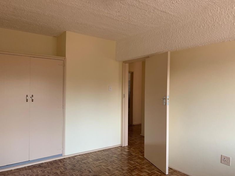 An empty bedroom featuring original parquet flooring, built-in cupboards, and a textured ceiling, offering a blank canvas for renovation.