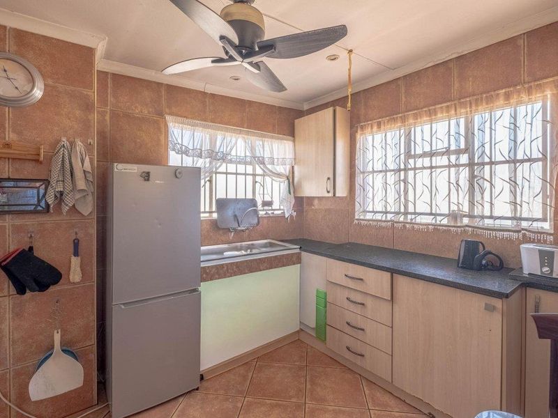 A functional kitchen featuring built-in cabinetry, laminate countertops, a stainless steel sink, and tiled finishes throughout, complete with security bars on the windows.