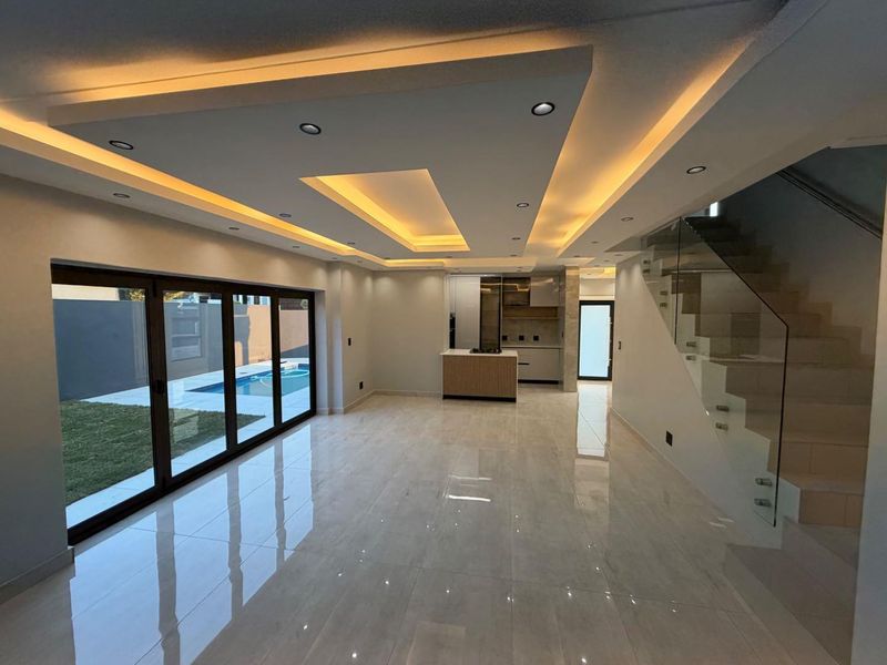 Spacious open-plan living area featuring modern recessed ceiling lighting, polished porcelain tiles, a glass staircase, and bi-fold doors opening to the pool area.