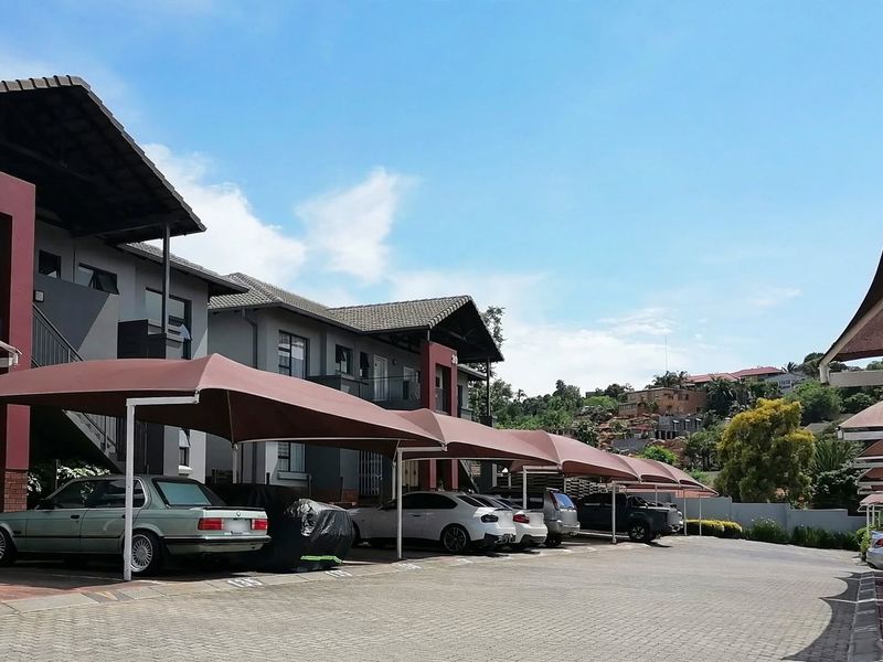 Exterior view of a townhouse complex featuring paved parking areas with shade cloth carports and multi-story residential units.