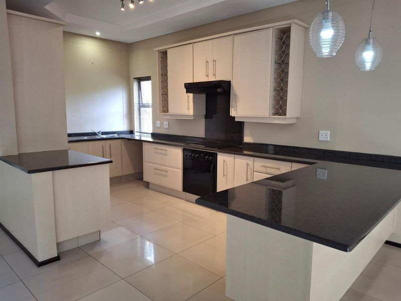 Modern kitchen featuring granite countertops, ample built-in cabinetry, integrated oven with extractor fan, and polished porcelain floor tiles in an open-plan layout.