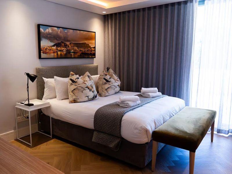 A modern, well-appointed bedroom featuring elegant herringbone timber flooring, recessed ceiling lighting, and floor-to-ceiling curtains for a sophisticated finish.