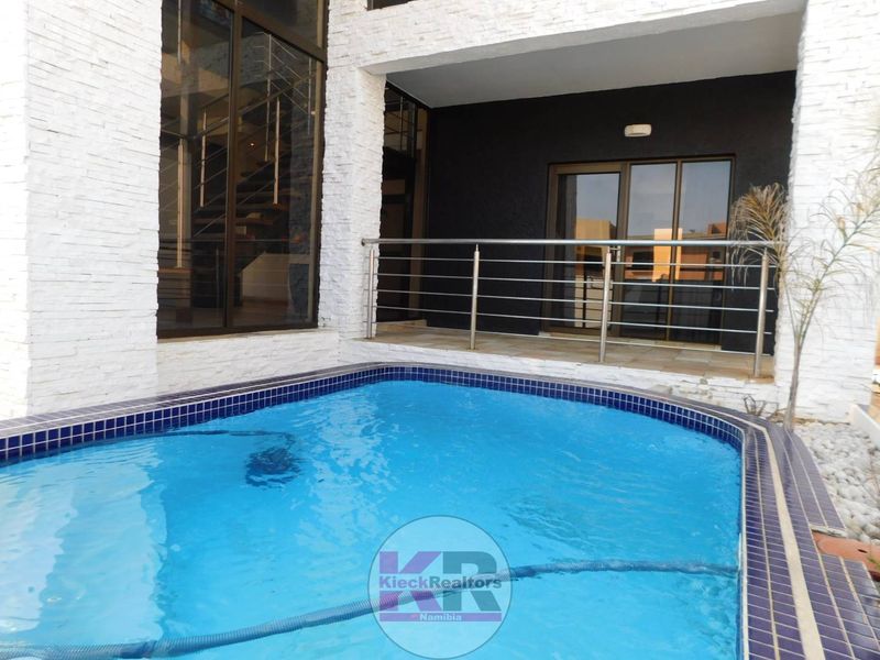 Outdoor pool area featuring a swimming pool with tiled coping, stainless steel balustrade, and modern stacked stone wall cladding.