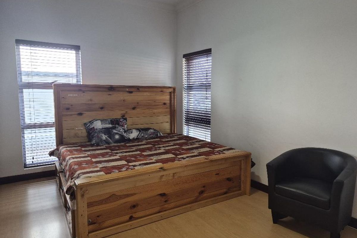 A bedroom featuring laminate flooring and two windows fitted with venetian blinds.