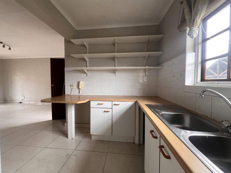 A dated kitchen featuring laminate countertops, open shelving, and a stainless steel double sink, offering a blank canvas for potential renovation and modernization.