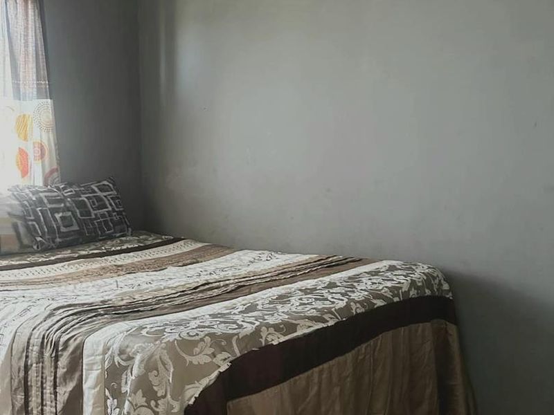 A bedroom featuring tiled flooring and grey painted walls, showing signs of wear and paint deterioration near the ceiling.