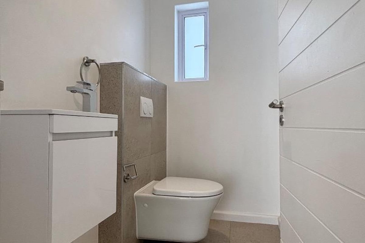 A modern guest cloakroom featuring a wall-mounted toilet, a sleek vanity basin, and neutral floor tiling.
