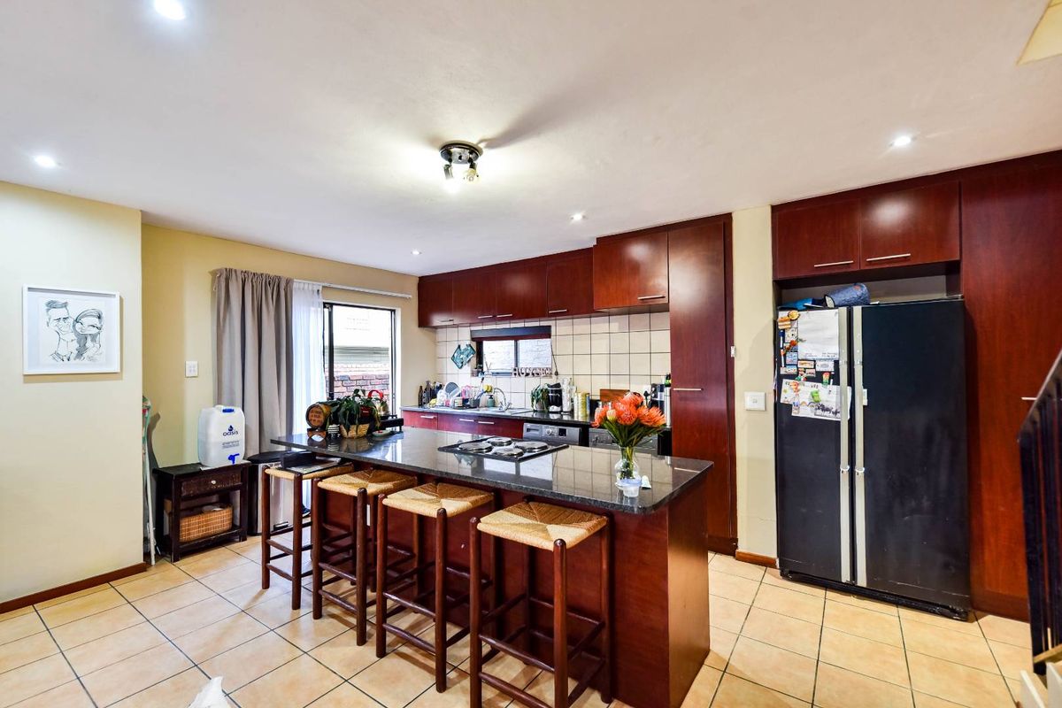 A functional kitchen featuring dark wood cabinetry, granite countertops, a central breakfast island with a built-in hob, and tiled flooring.