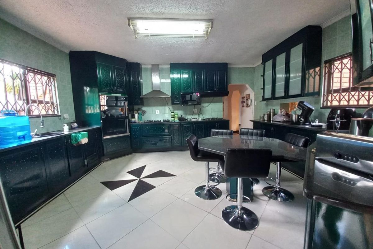 Spacious kitchen featuring dark cabinetry, built-in oven, extractor fan, and a central dining area with tiled flooring.