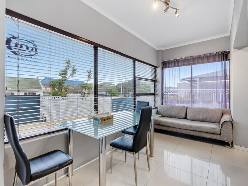 A bright living area featuring large windows with venetian blinds, neutral tiled flooring, and a modern ceiling light fixture.