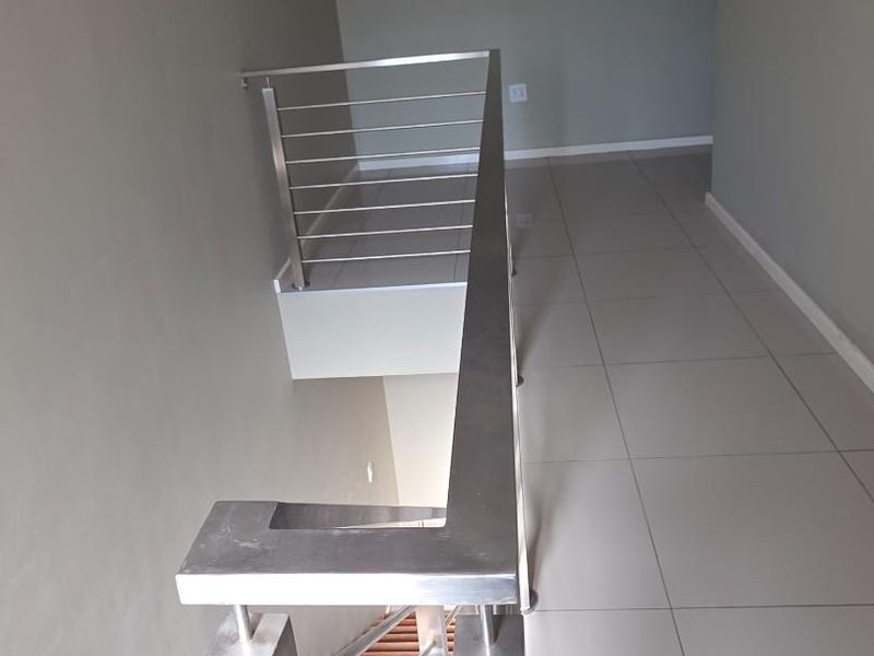 A bright hallway featuring a modern stainless steel balustrade and wooden staircase with neutral tiled flooring.