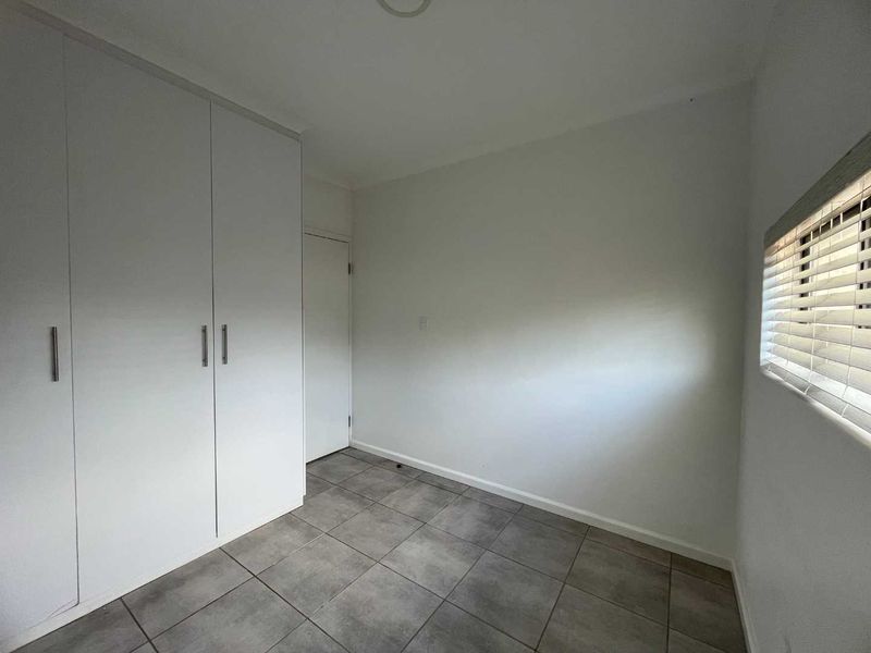A clean, empty bedroom featuring neutral tiled flooring, built-in wardrobes, and venetian blinds, offering a blank canvas for personalization.
