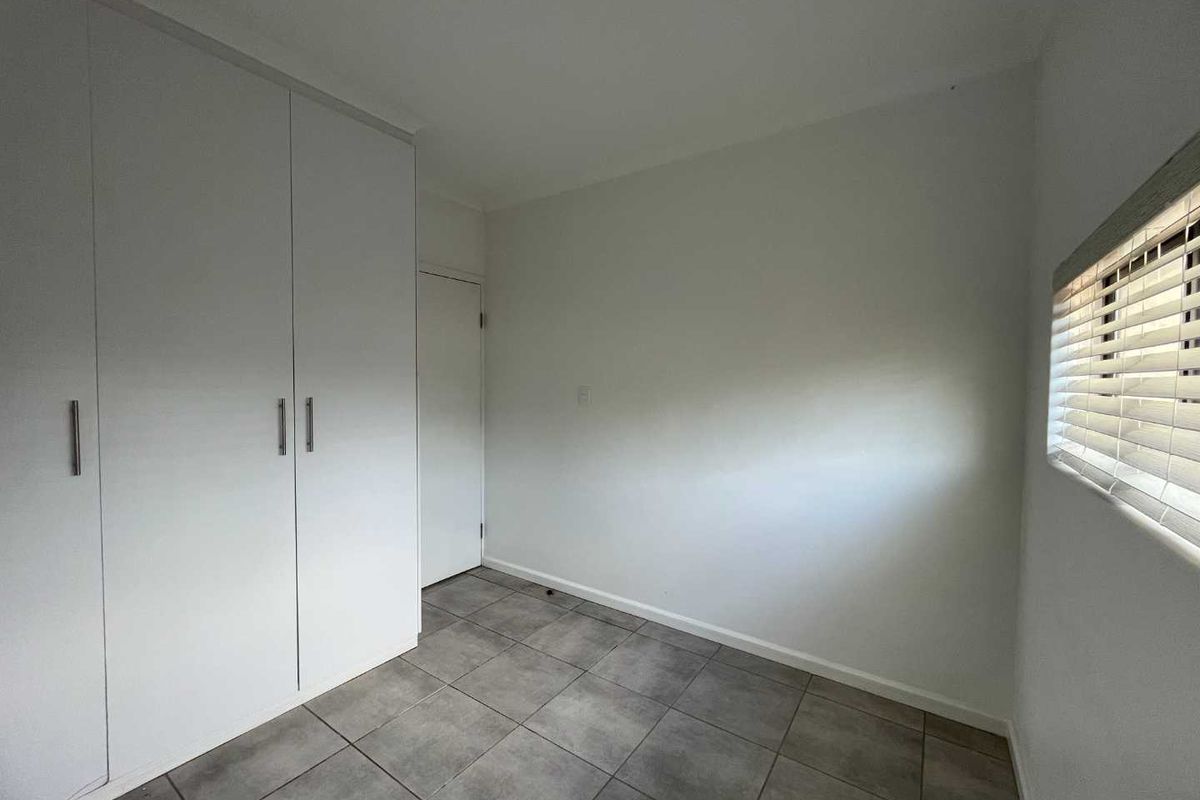 A clean, empty bedroom featuring neutral tiled flooring, built-in wardrobes, and venetian blinds, offering a blank canvas for personalization.