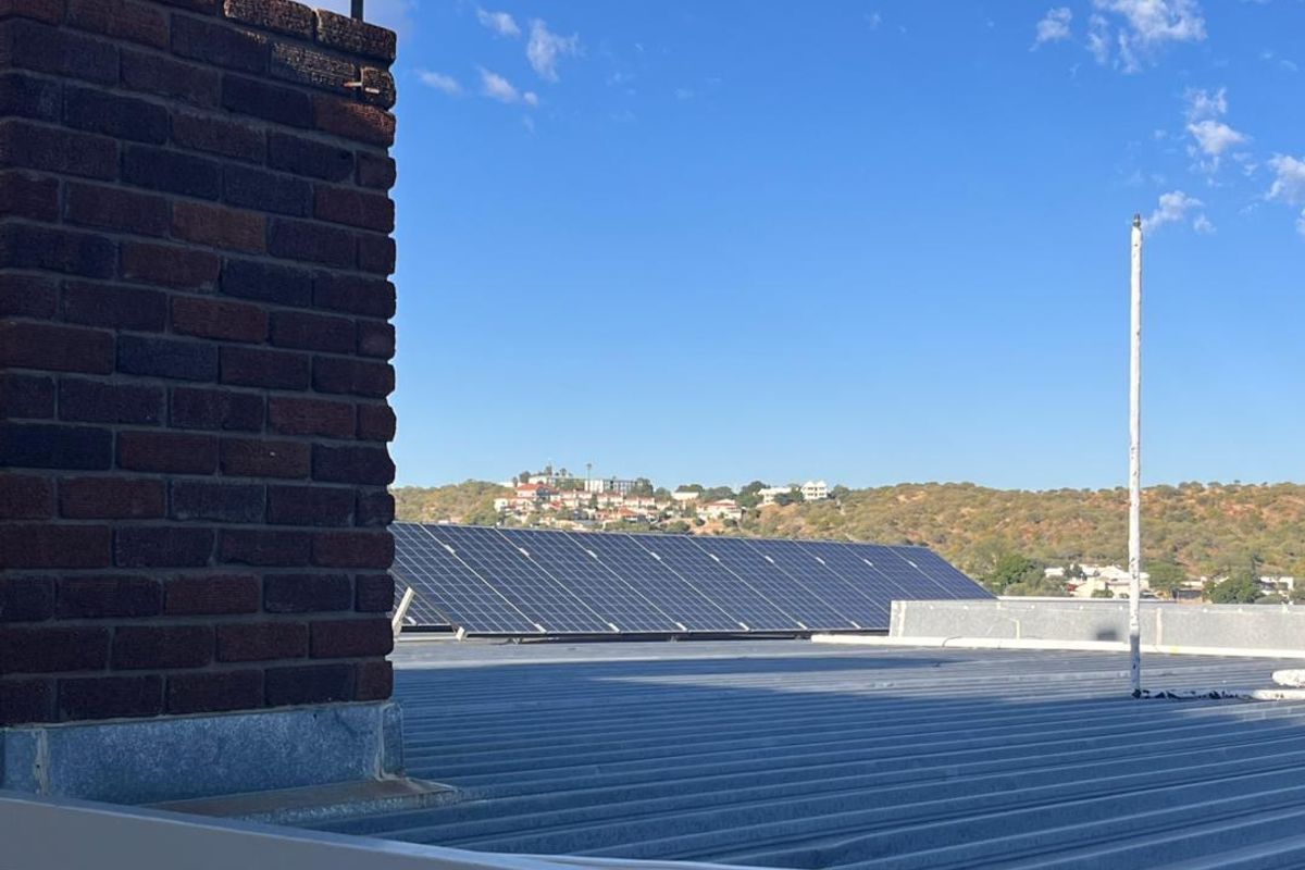 View from the roof showing a corrugated metal roof, a brick chimney stack, and a large array of solar panels.