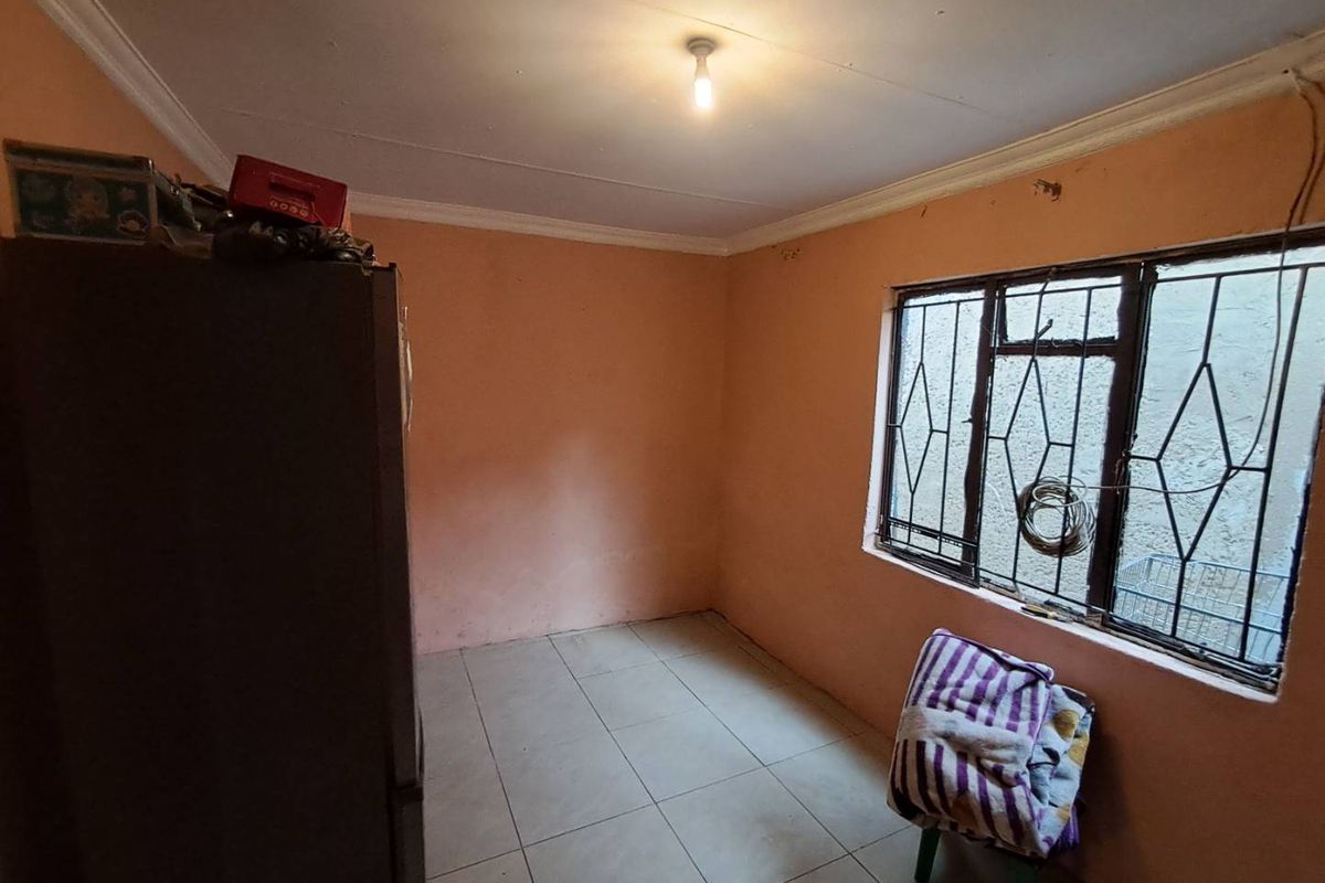 A compact bedroom featuring tiled flooring, peach-toned walls, and a window fitted with security bars.