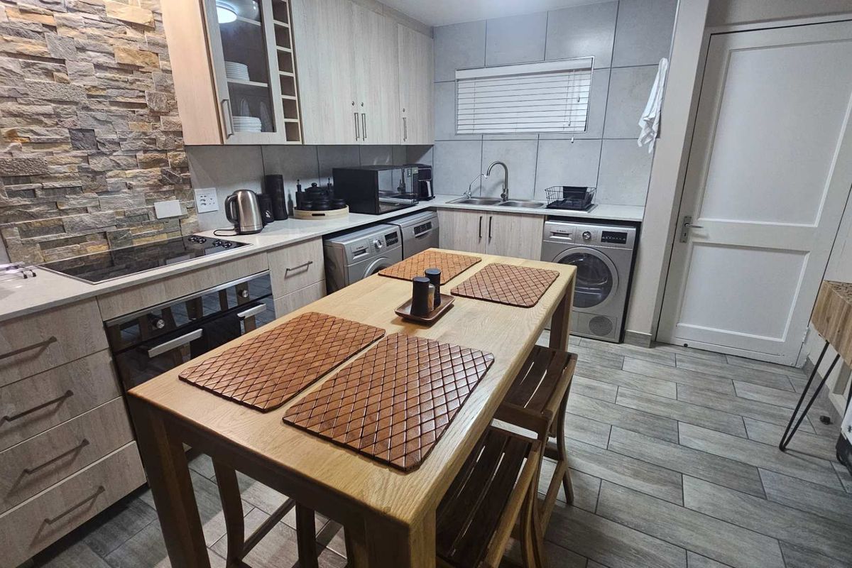 Modern kitchen featuring light wood cabinetry, stone veneer accent wall, integrated appliances, and tiled flooring with a functional layout.