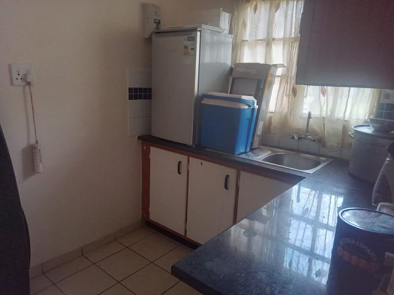 A compact kitchen area featuring built-in cabinetry, a stainless steel sink, and tiled flooring, currently showing signs of age and wear.