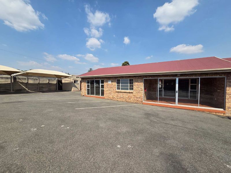 Front exterior view of a facebrick office building featuring a paved parking area, shade cloth carports, and aluminium sliding door entrances.