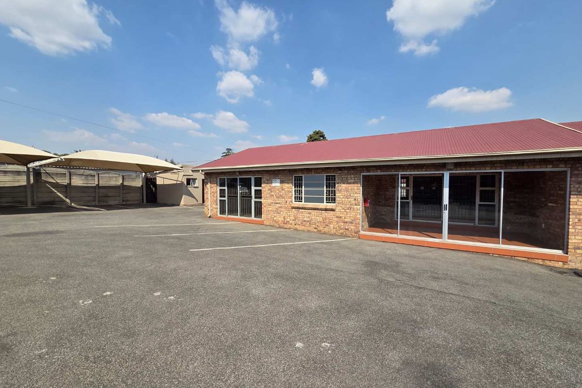 Front exterior view of a facebrick office building featuring a paved parking area, shade cloth carports, and aluminium sliding door entrances.