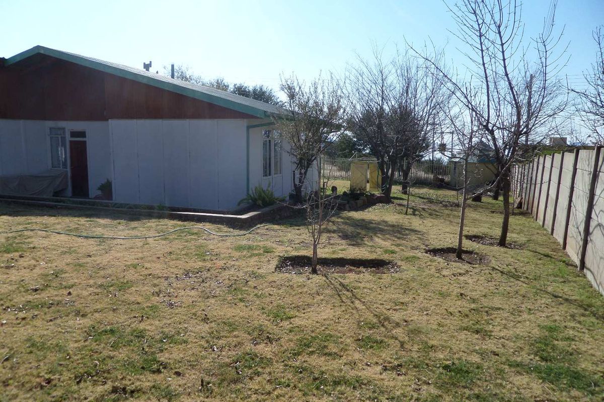 A view of the rear garden and side elevation of the house, featuring a large lawn area and perimeter boundary wall.