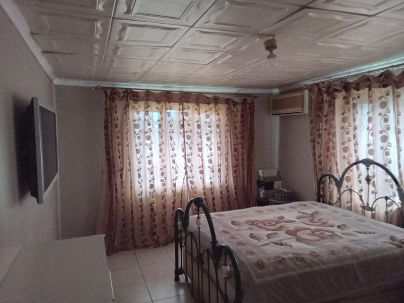 A bedroom featuring tiled flooring, a window-mounted air conditioning unit, and a decorative tiled ceiling.