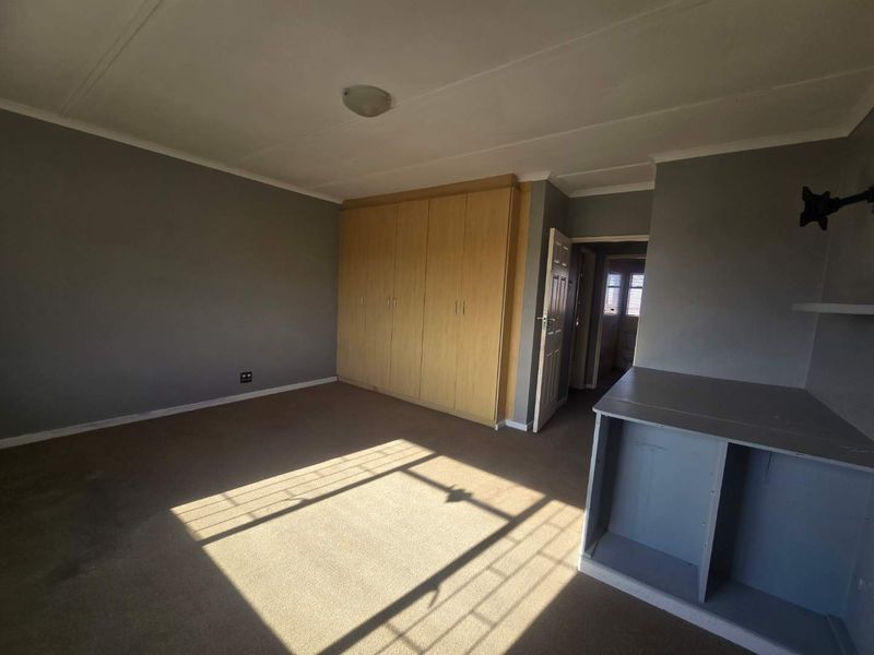 A spacious bedroom featuring built-in wooden cupboards, carpeted flooring, and a built-in shelving unit, offering a blank canvas for personalization.