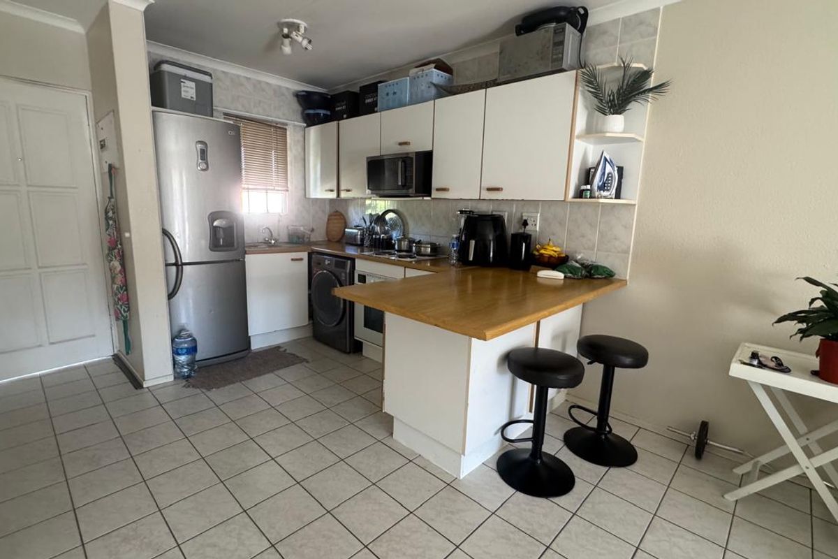 Compact kitchen featuring white cabinetry, a wooden breakfast bar, tiled flooring, and integrated appliances, offering a functional layout for daily use.