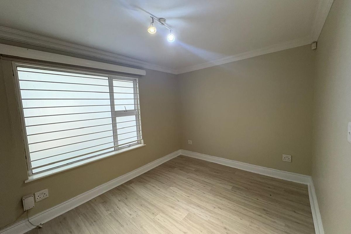 A bright, empty bedroom featuring light wood-look laminate flooring, neutral wall paint, crown molding, and fitted window blinds.