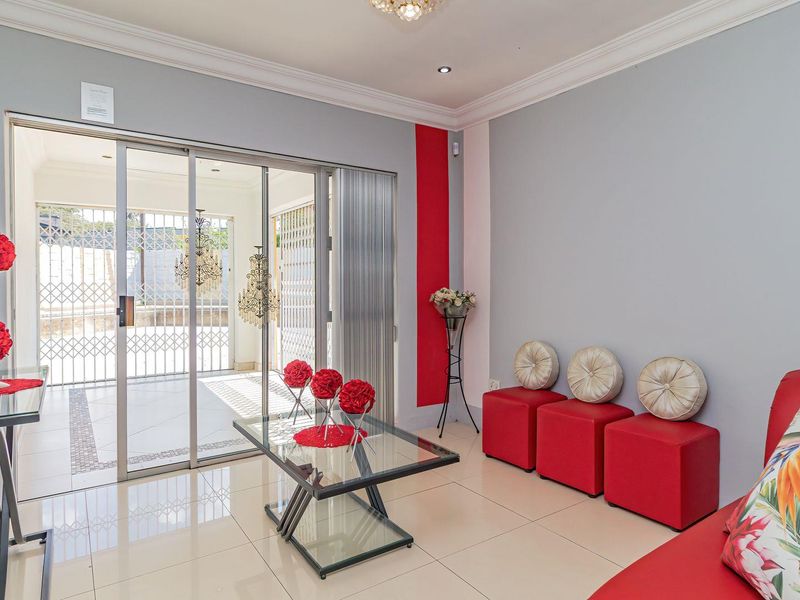 A bright living room featuring tiled flooring, decorative ceiling cornices, and large sliding glass doors that open onto a covered patio area.