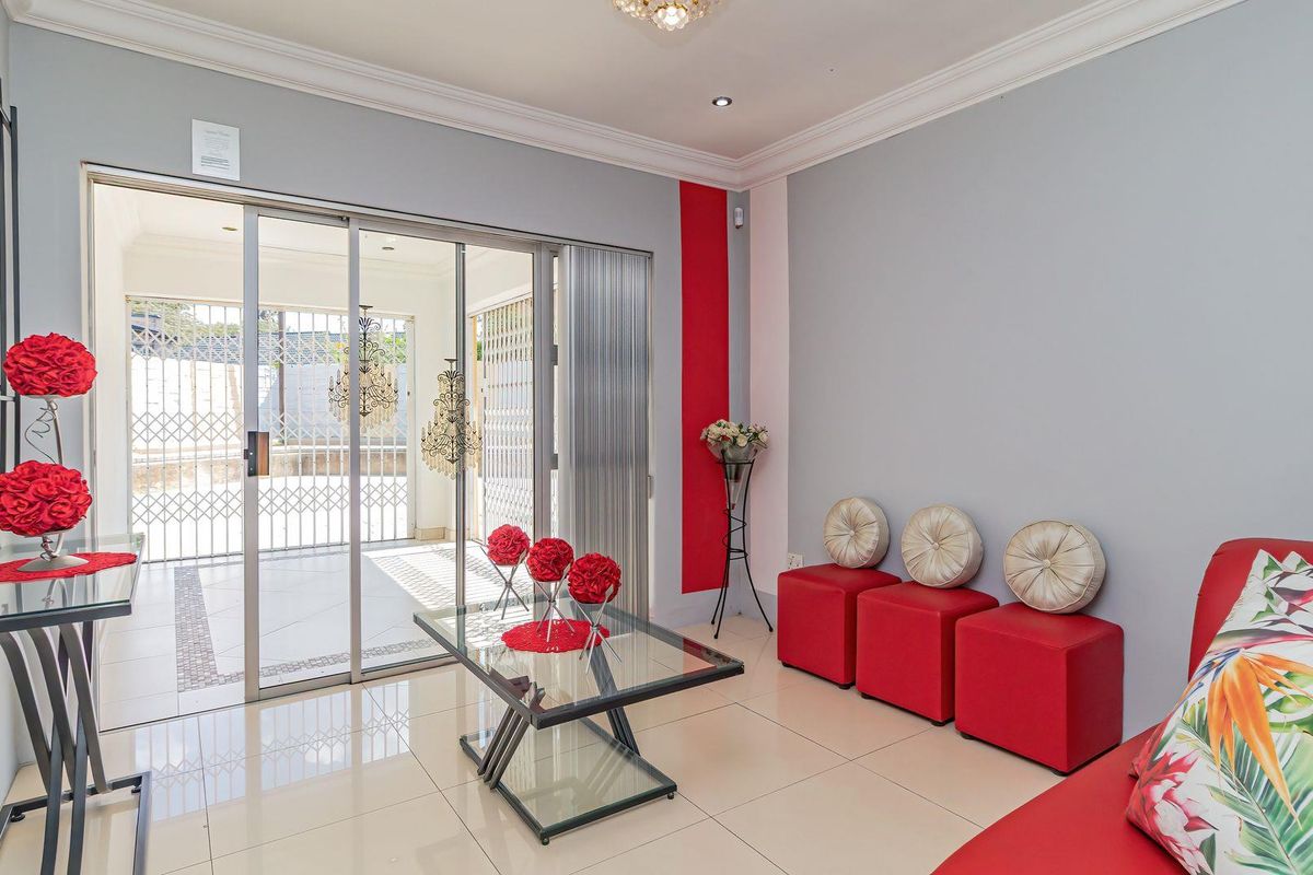 A bright living room featuring tiled flooring, decorative ceiling cornices, and large sliding glass doors that open onto a covered patio area.