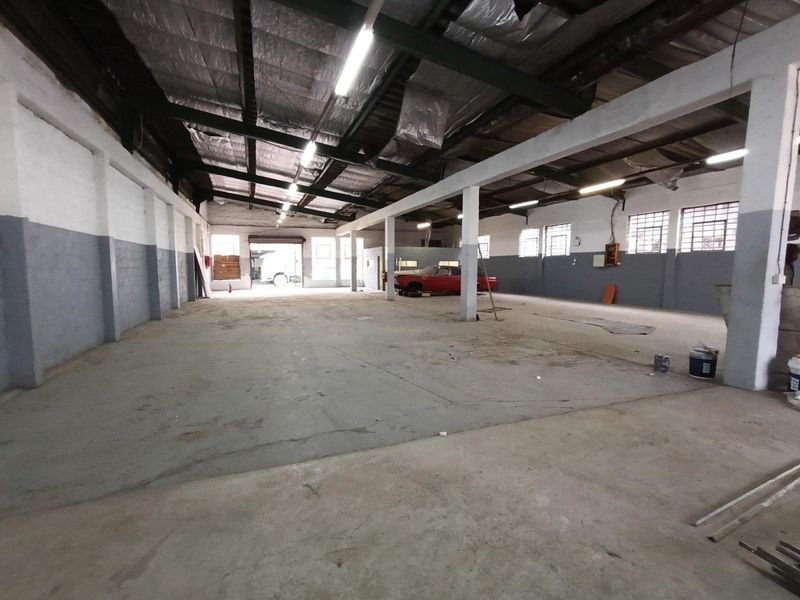 Spacious industrial warehouse or workshop area featuring high ceilings with exposed steel trusses, concrete flooring, and ample natural light through steel-framed windows.