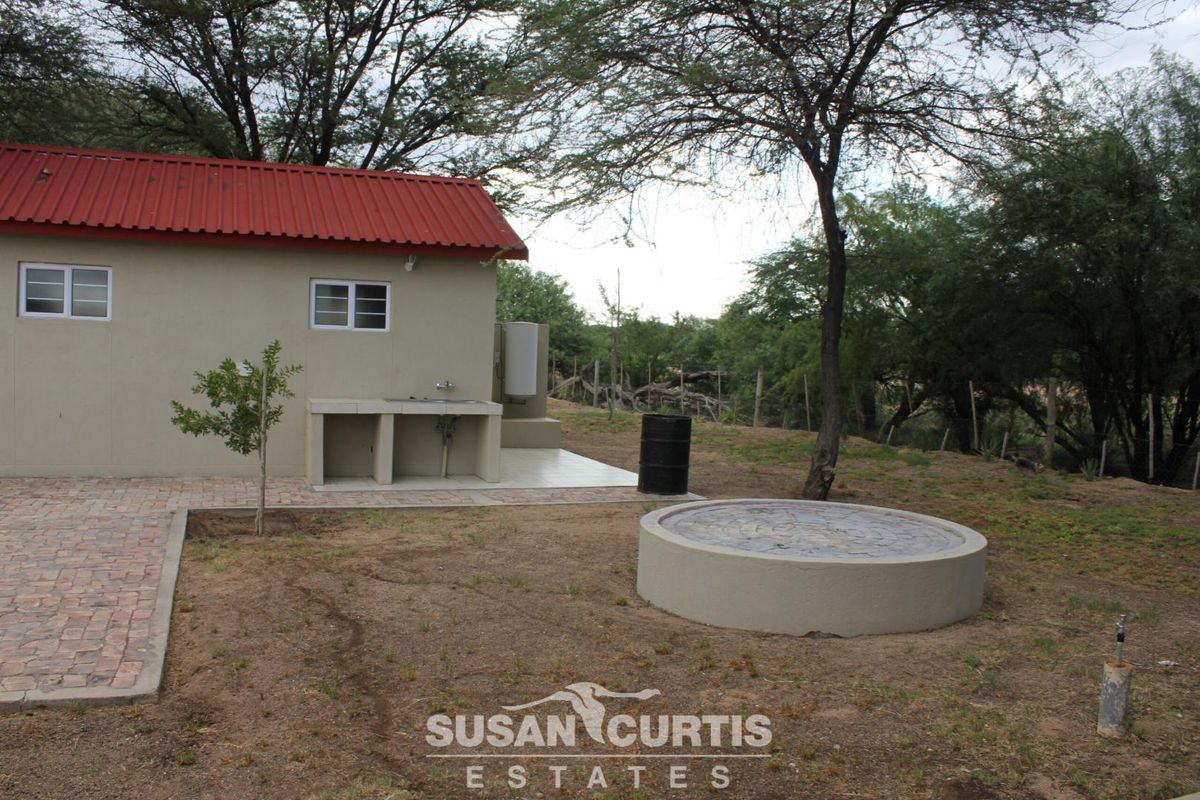 Exterior view of a lodge building featuring a red corrugated metal roof, an outdoor prep area with sink, and a circular concrete water reservoir.