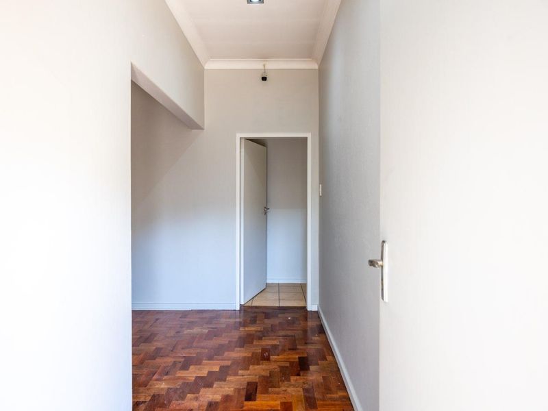 A clean, empty hallway featuring classic parquet flooring and coved ceiling details, providing a neutral transition space between rooms.