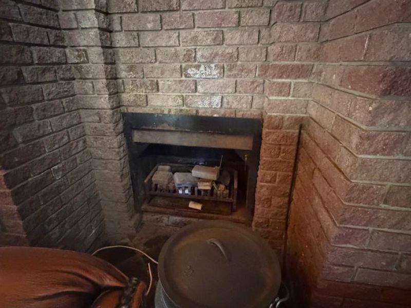 A rustic living room area featuring a prominent brick fireplace and built-in hearth, providing a traditional focal point for the space.