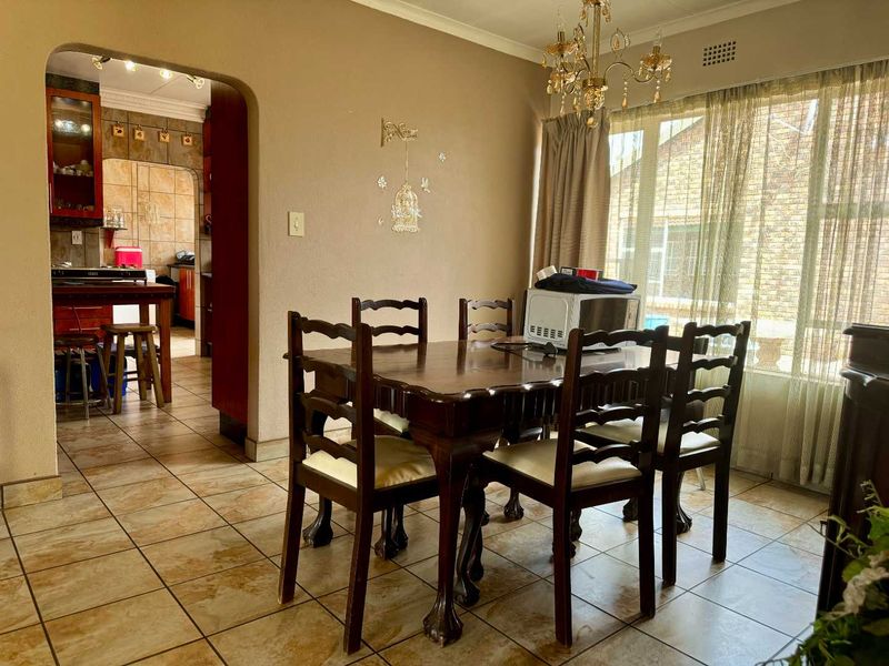 A dining room featuring tiled flooring, a coved ceiling, and a decorative chandelier, with an open archway leading into the adjacent kitchen area.