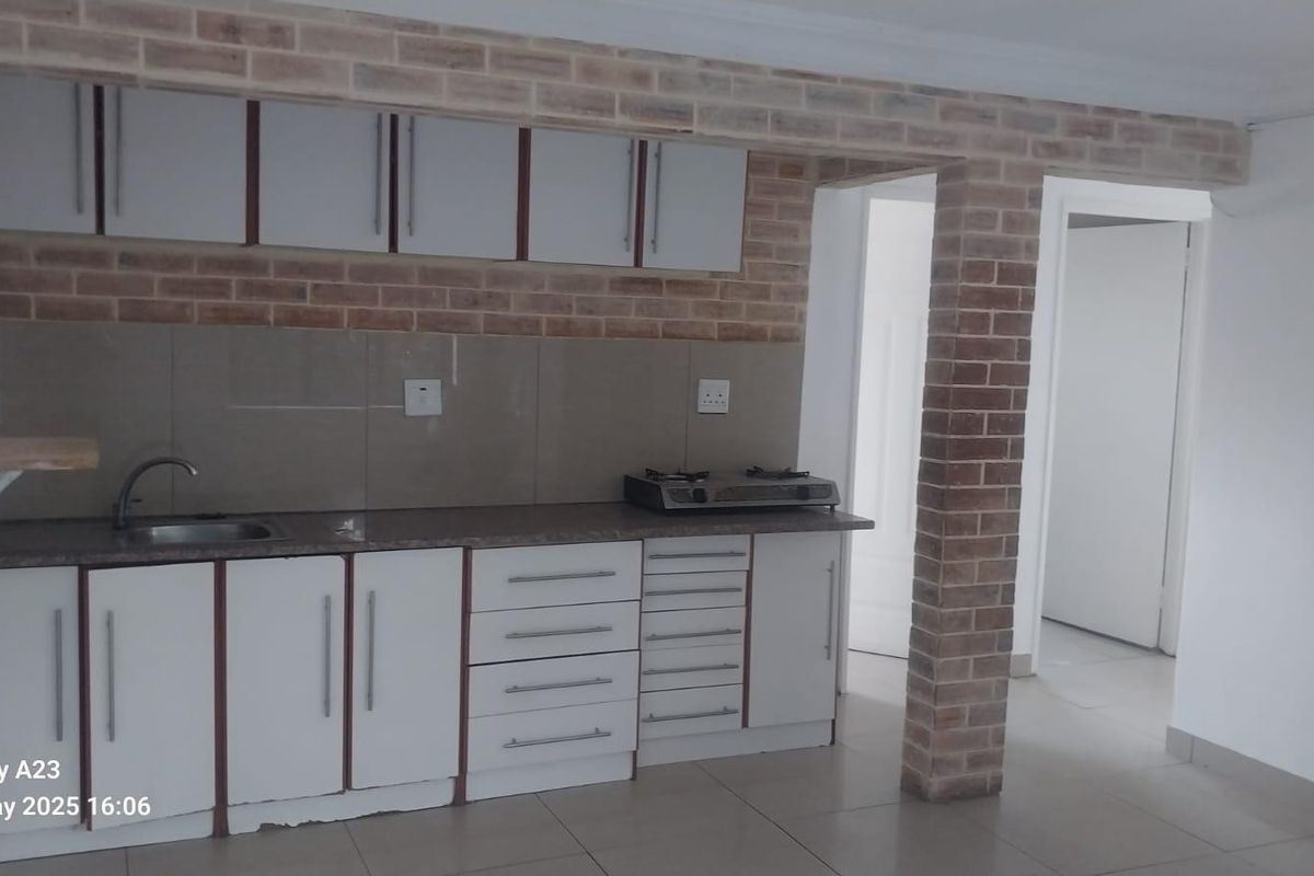 A functional kitchen featuring white cabinetry, a laminate countertop, stainless steel sink, and a distinctive exposed brick feature wall.
