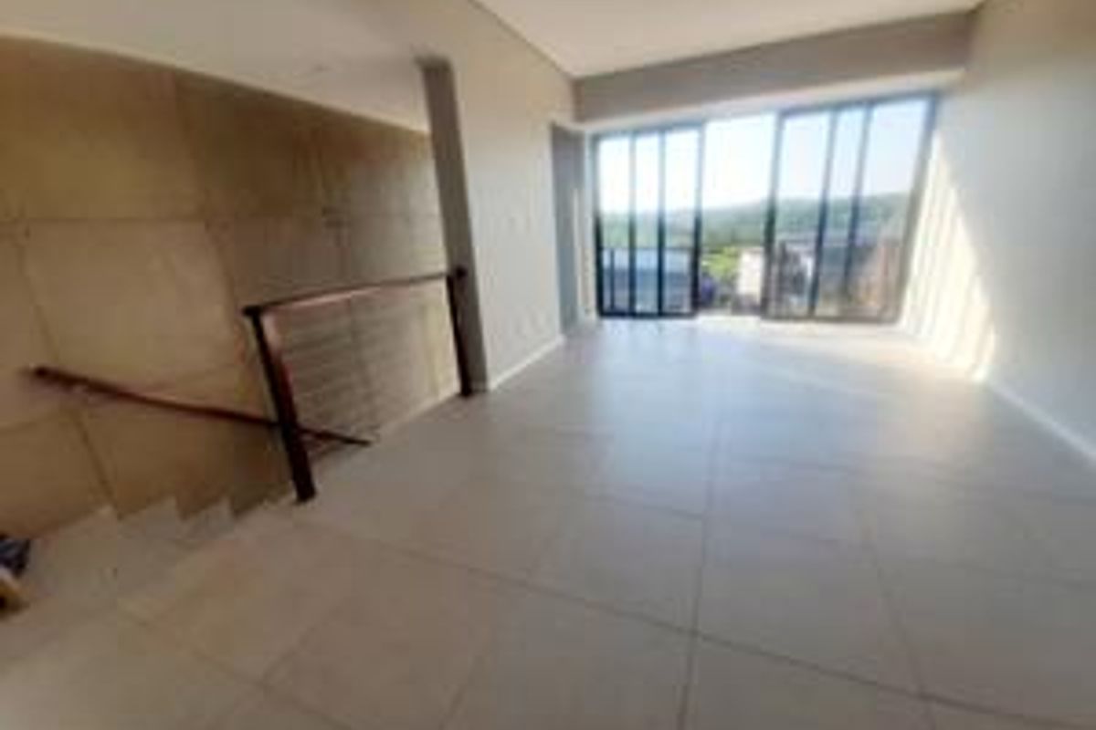 Spacious open-plan living area featuring large format floor tiles, a feature wall, and sliding glass doors leading to an outdoor view.