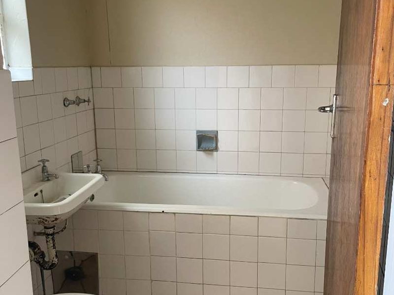 A dated bathroom featuring a standard bathtub, wall-mounted basin, and toilet, requiring significant renovation and modernization of fixtures and finishes.