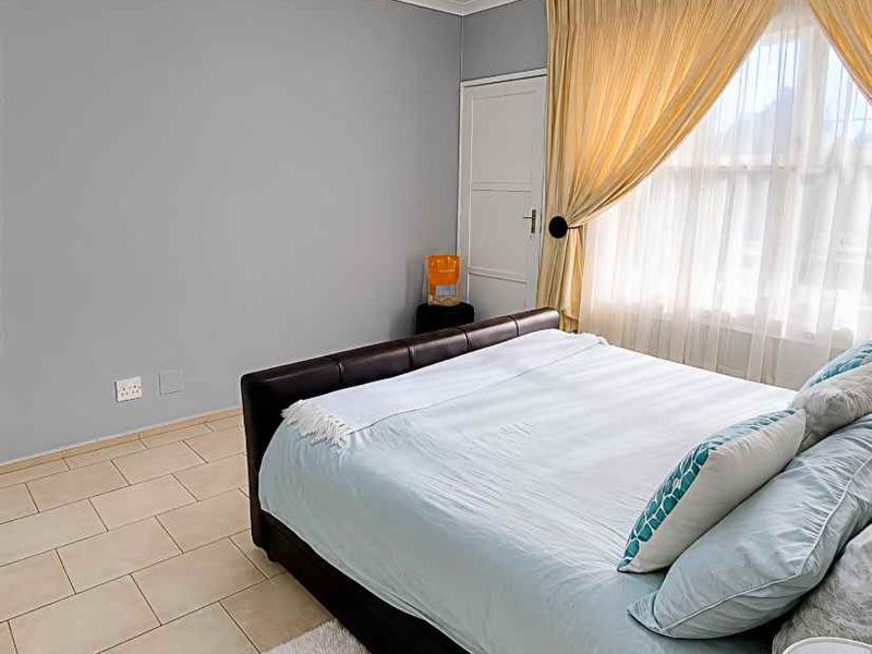 A bedroom featuring tiled flooring, neutral wall paint, and a window with curtains.