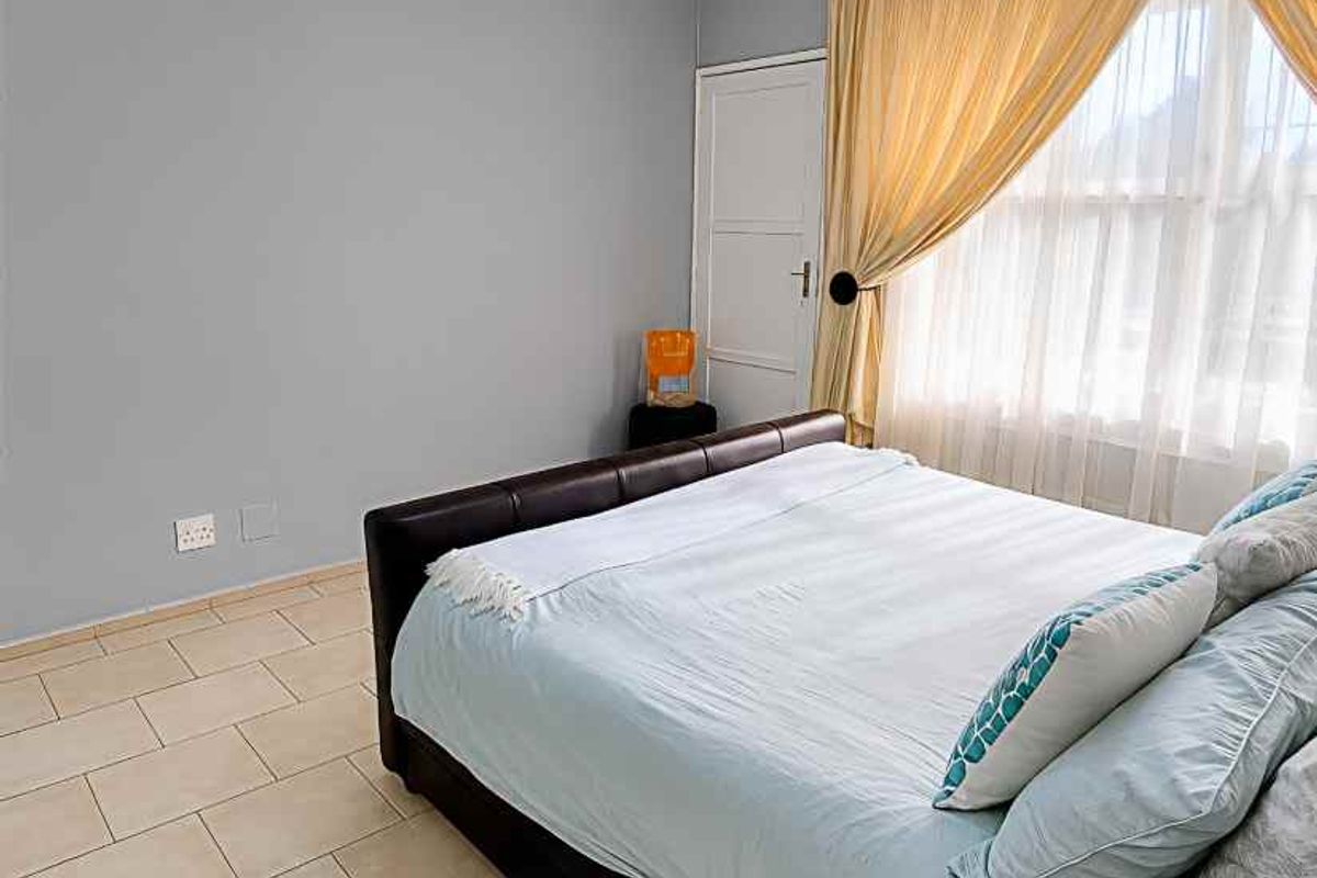 A bedroom featuring tiled flooring, neutral wall paint, and a window with curtains.
