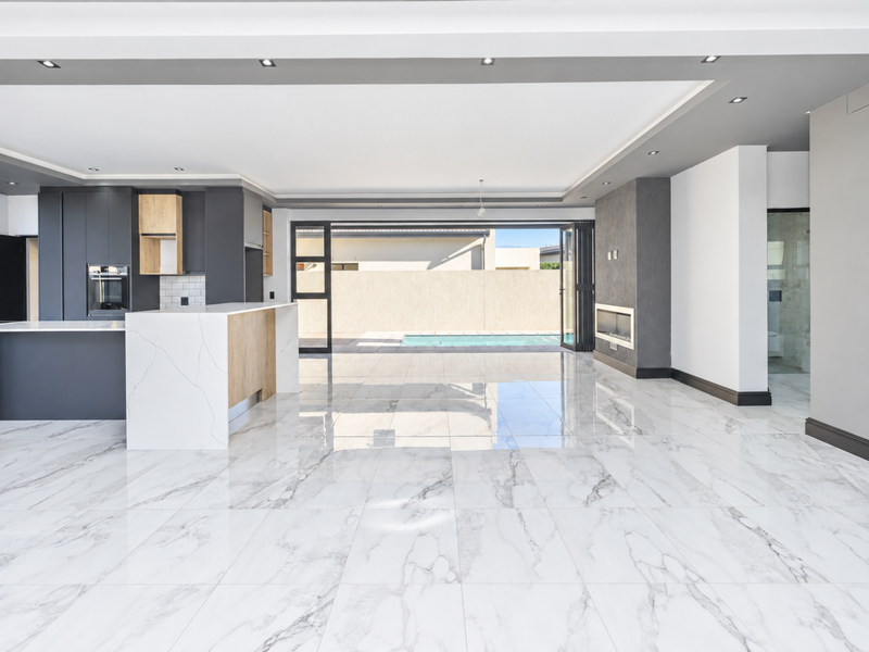 Spacious open-plan living area featuring high-end marble-look flooring, a modern kitchen with built-in appliances, and seamless flow to the outdoor pool area.