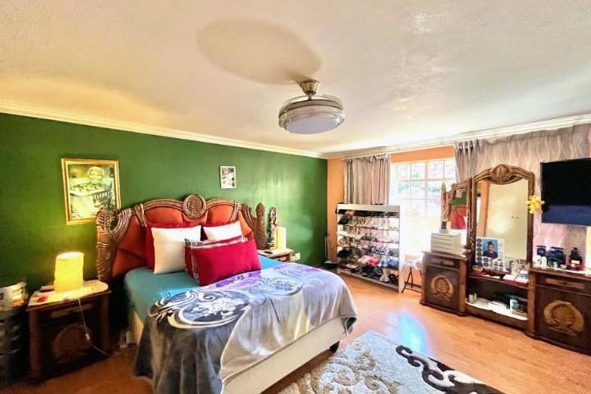 A spacious bedroom featuring laminate flooring, a ceiling fan, and a large window with curtains.