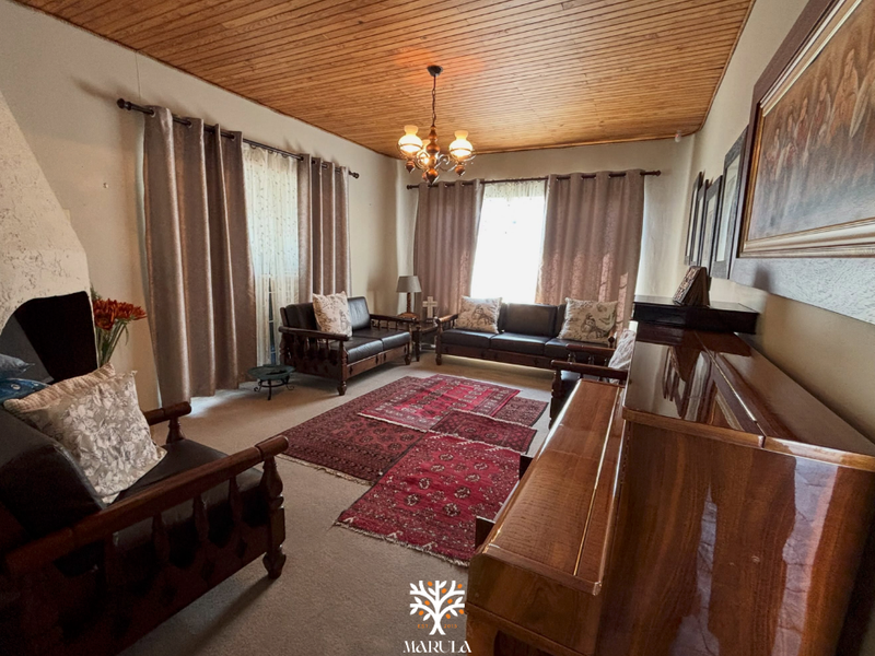 A cozy living room featuring a warm timber-clad ceiling, a built-in fireplace, and classic chandelier lighting, offering a traditional and inviting atmosphere.